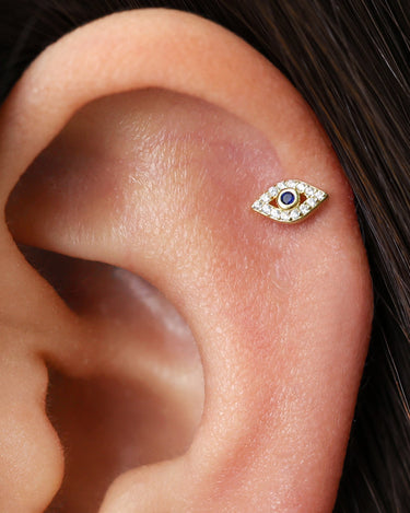 Evil eye push pin earrings paved with diamonds and sapphire birthstones as helix earrings on model.